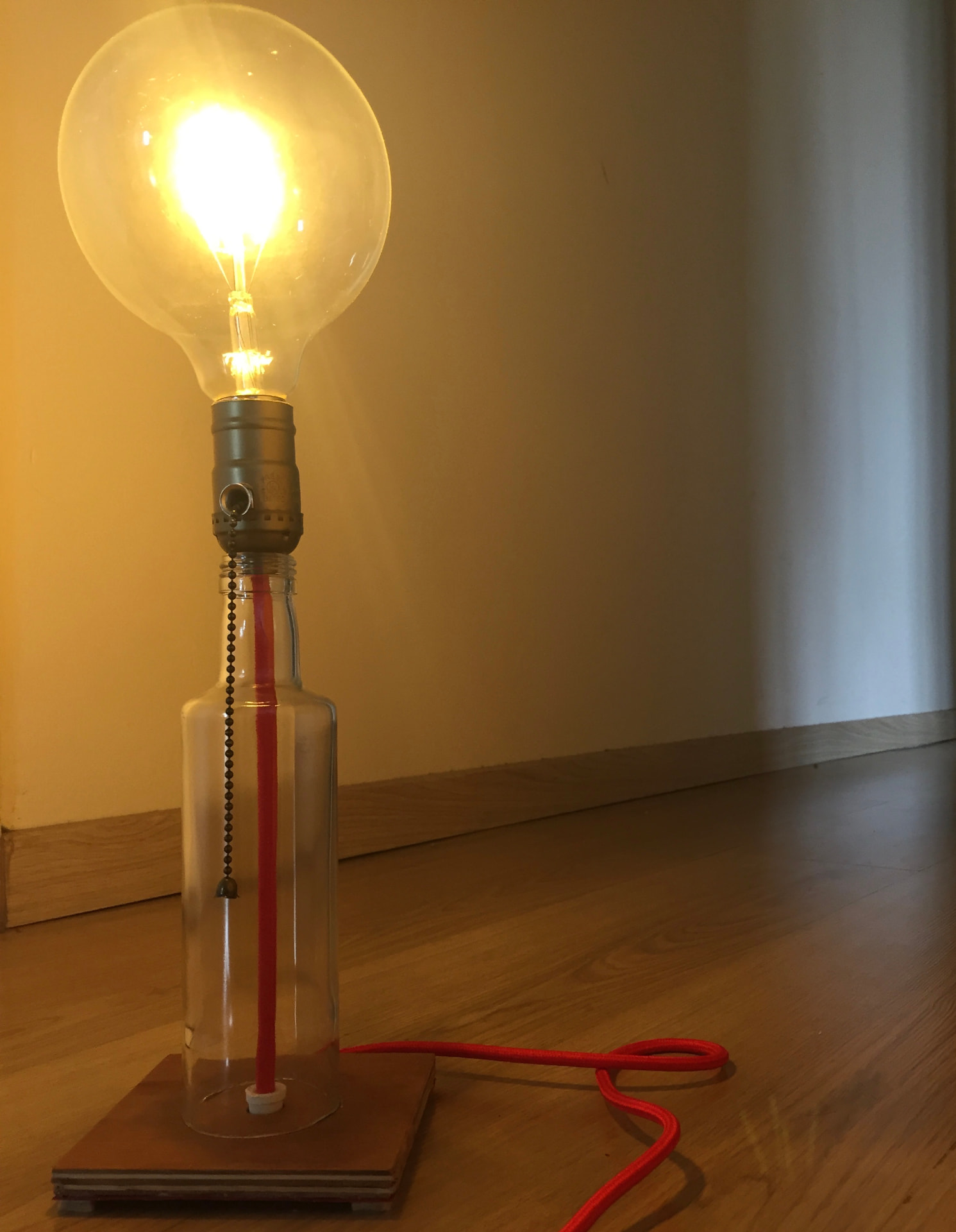 Lamp 05, Upcycled bottle, plywood base, brass socket, red textile cord, globe bulb